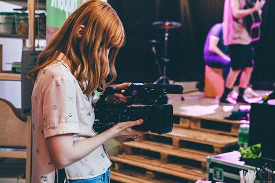 Photo of a student filming a scene with a handheld camera. 