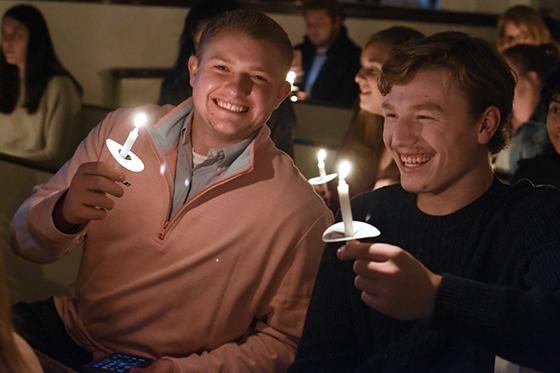 Photo of two Chatham University students smiling while holding candles in a candlelit chapel service on campus. 